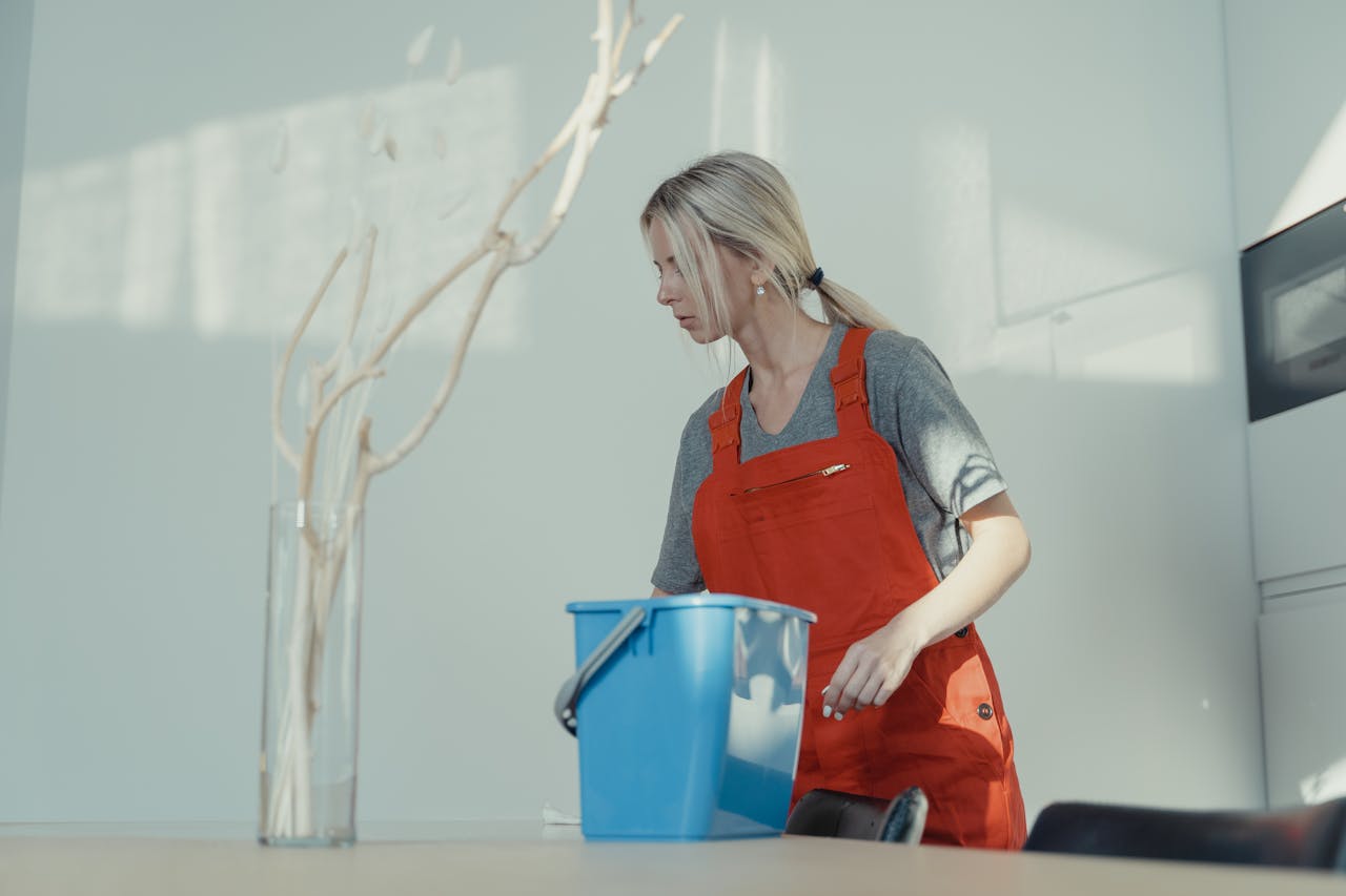 hero-img-02 A woman in a red uniform cleans indoors with a blue bucket, ensuring a spotless environment.
